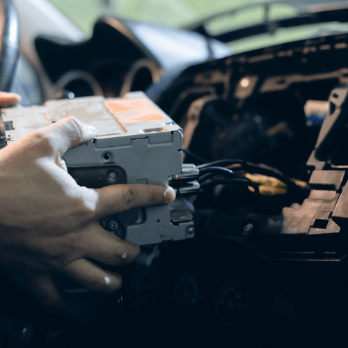 Hands installing a car stereo unit inside a vehicle dashboard, with wiring exposed