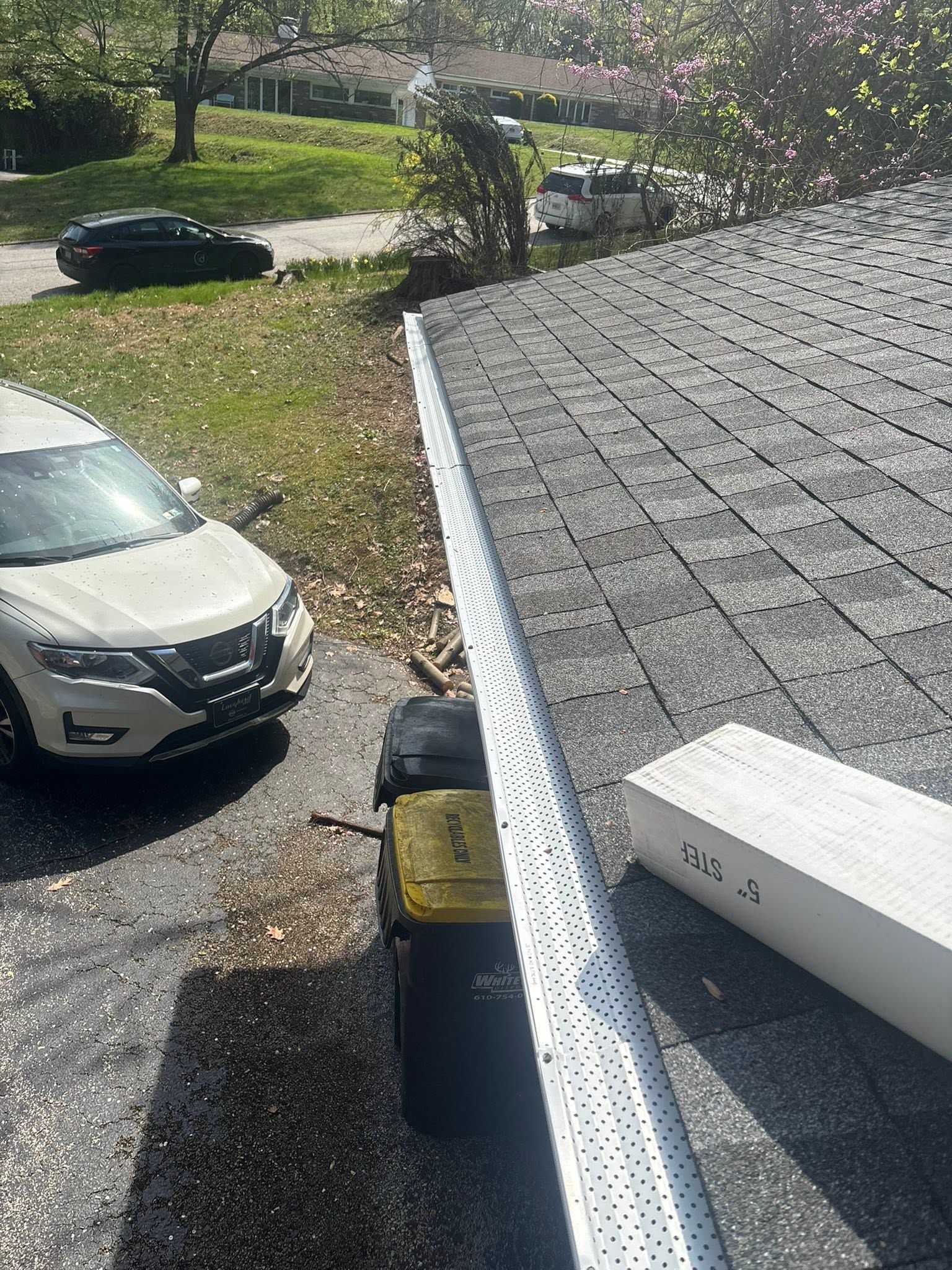 View from a roof edge over a driveway with parked cars and a yard in daylight