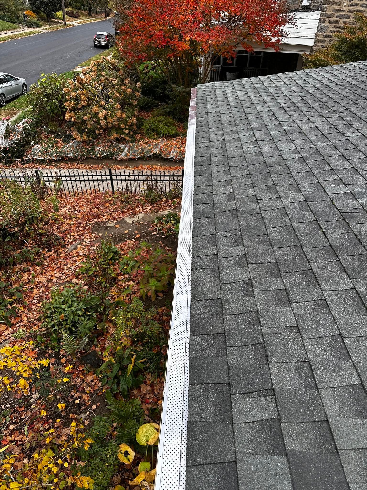 Roof overlooking autumn garden and roadside, with gray shingles and red-orange foliage below