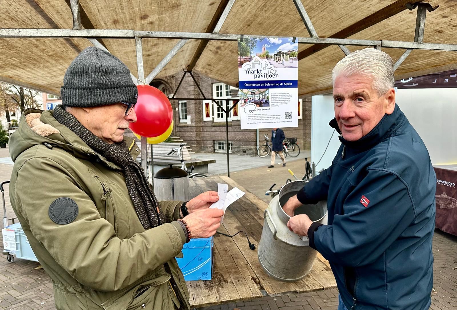 Twee mannen staan ​​onder een tent met elkaar te praten.