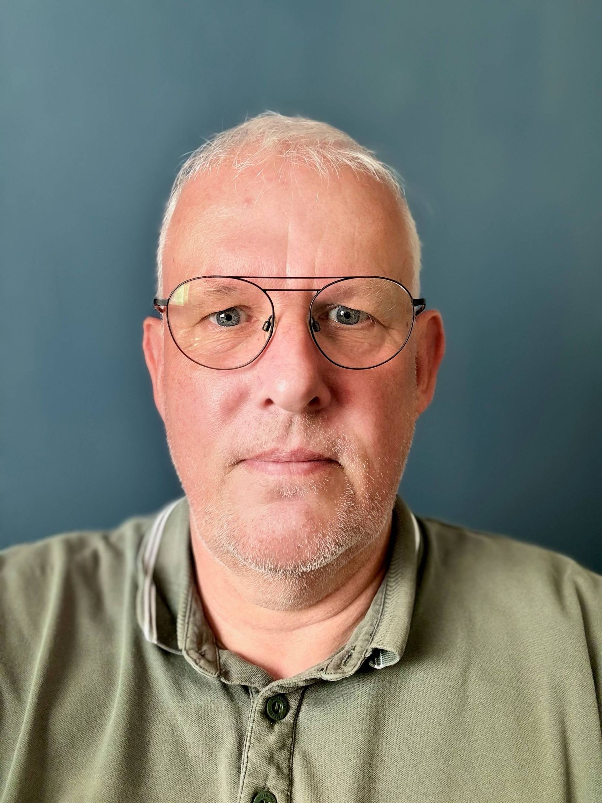 Een man met een bril en een groen shirt kijkt naar de camera.
