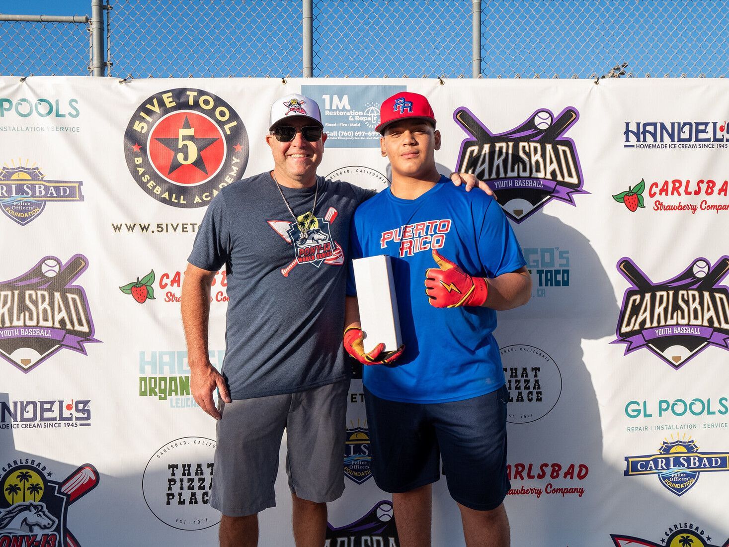 Two men posing with a trophy in front of sponsor banners at a sports event