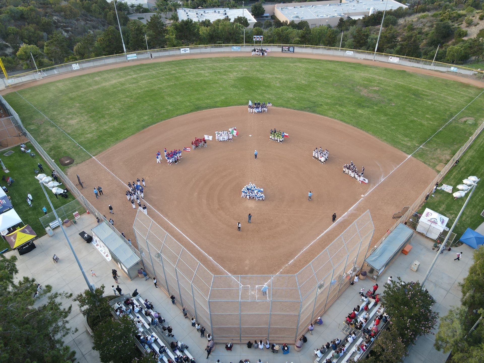 Aerial view of a baseball field with teams gathered near home plate and spectators along the fence
