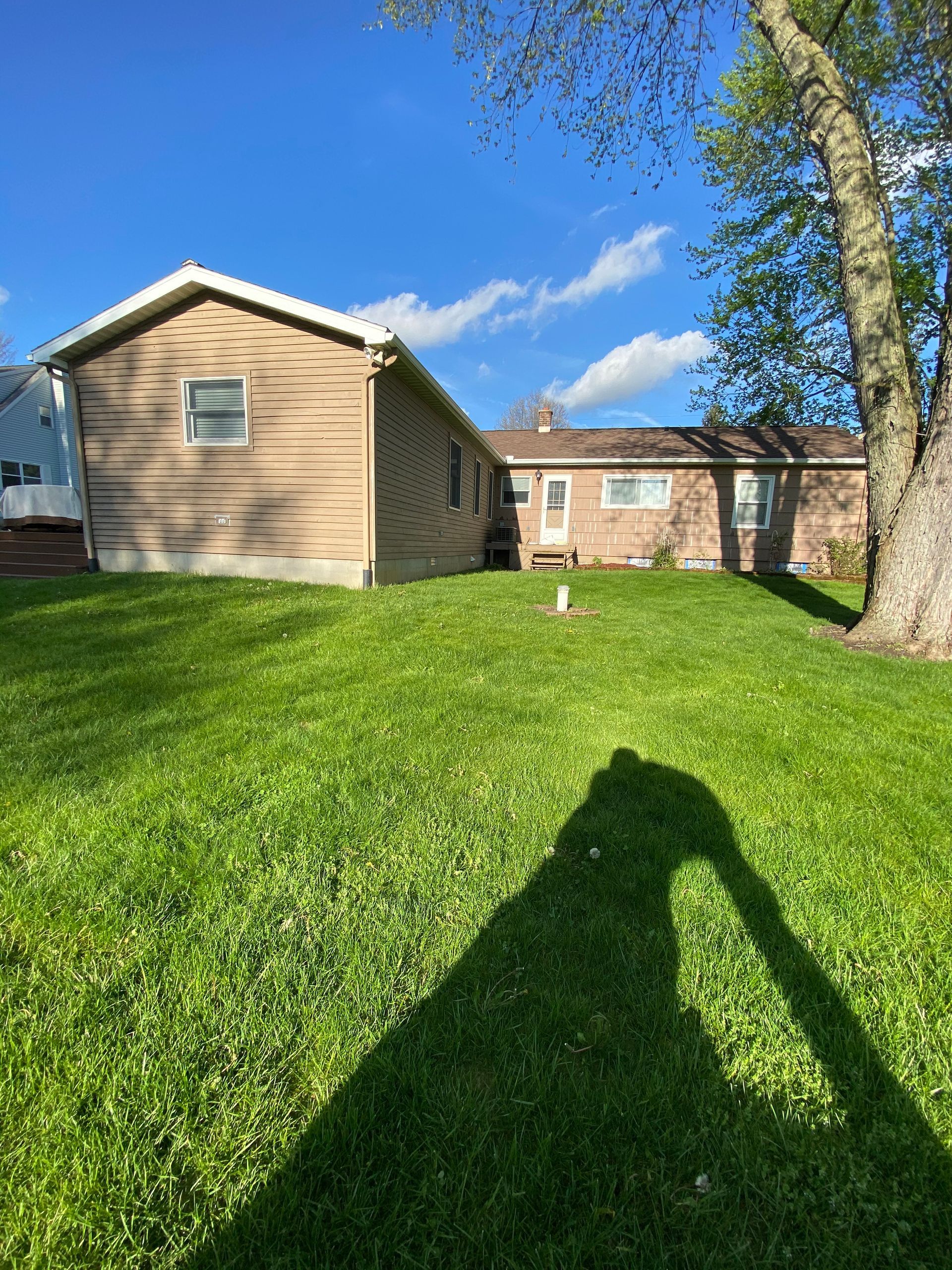 A shadow of a person is cast on the grass in front of a house.