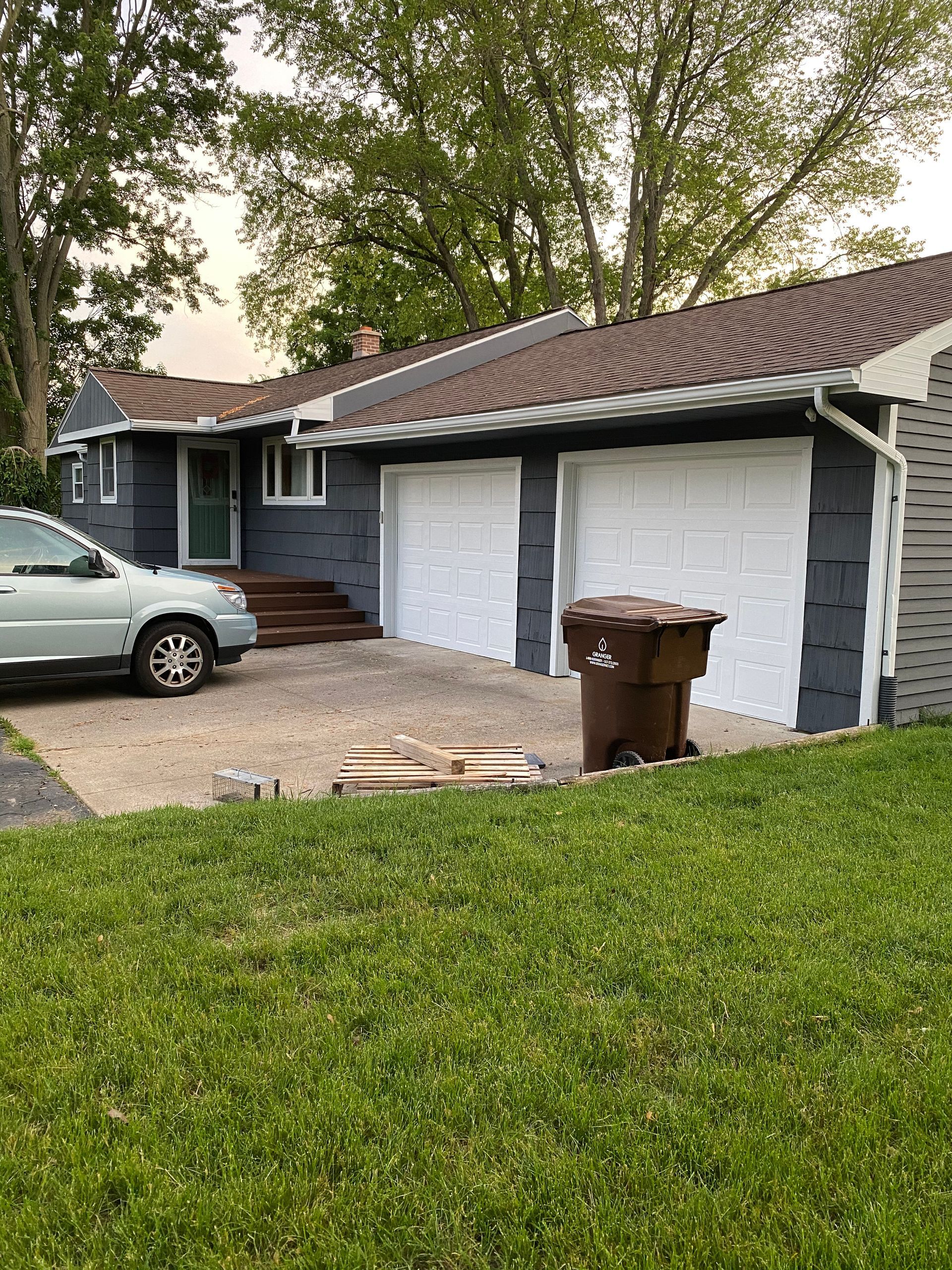A car is parked in front of a house with two garage doors.