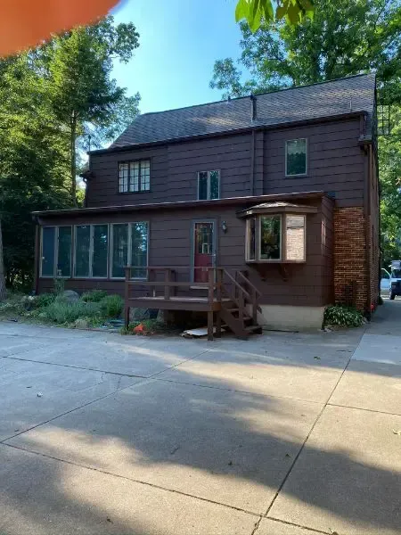 A large brown house with a lot of windows is surrounded by trees.