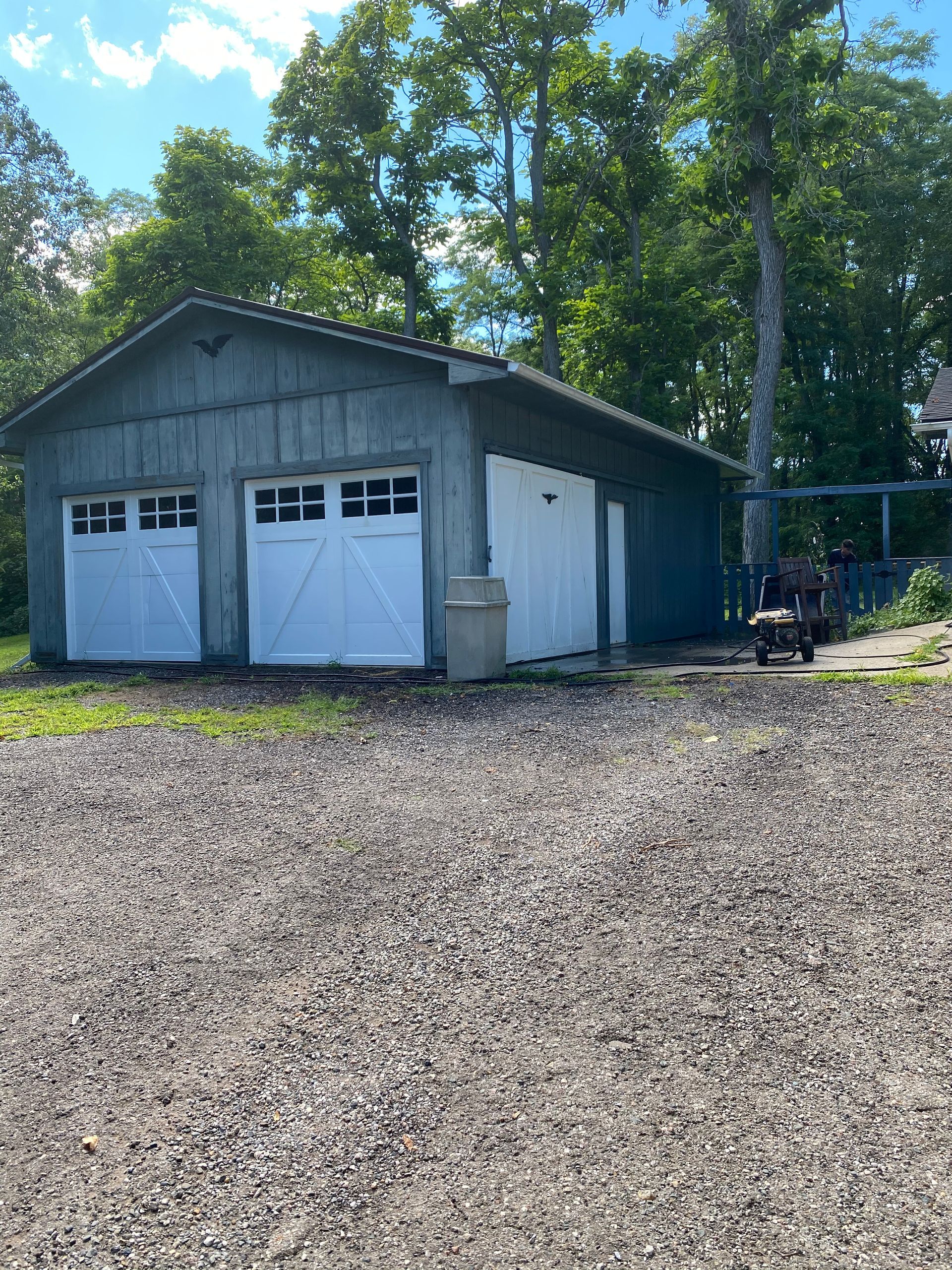 A garage with two white garage doors and a gravel driveway in front of it
