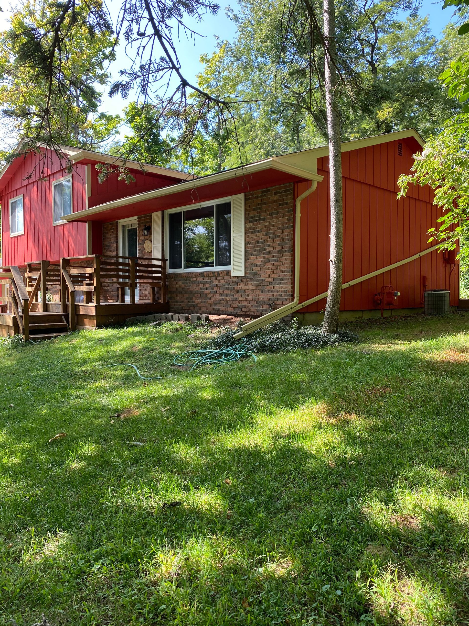 A red house is sitting in the middle of a lush green field.