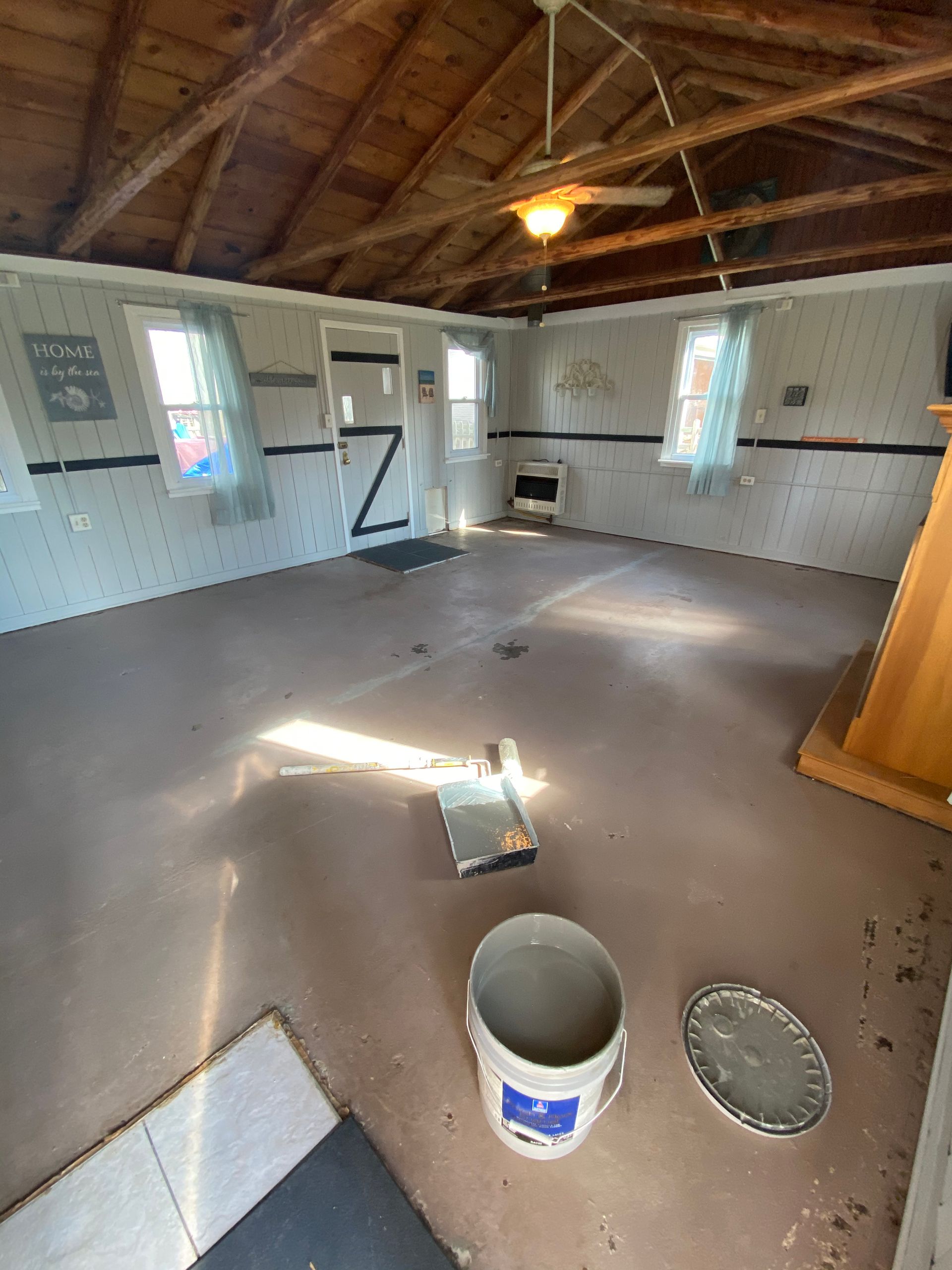 An empty room with a ceiling fan and a bucket on the floor.