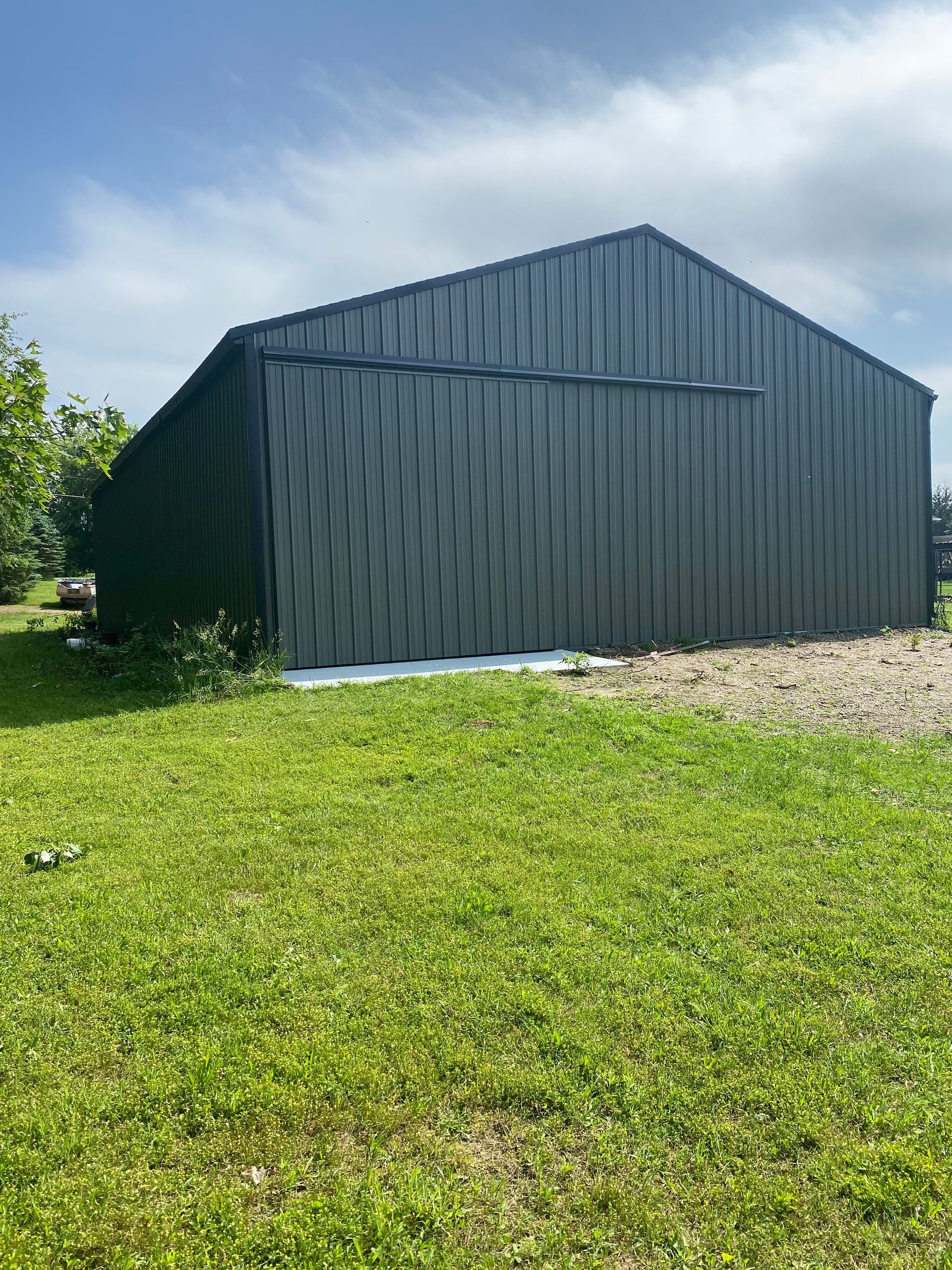 A large black barn is sitting in the middle of a lush green field.