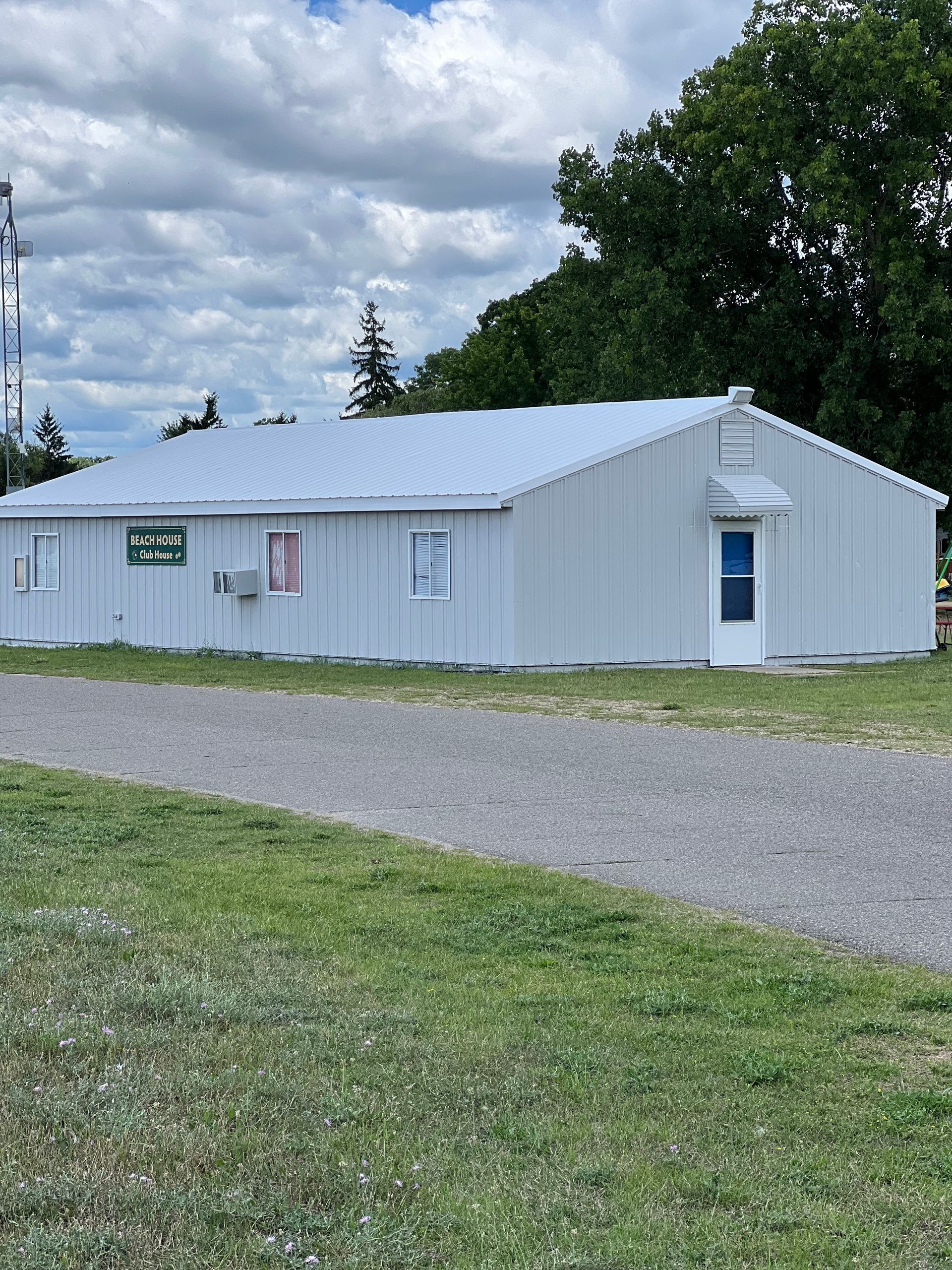 A white building with a blue door is sitting in the middle of a grassy field.