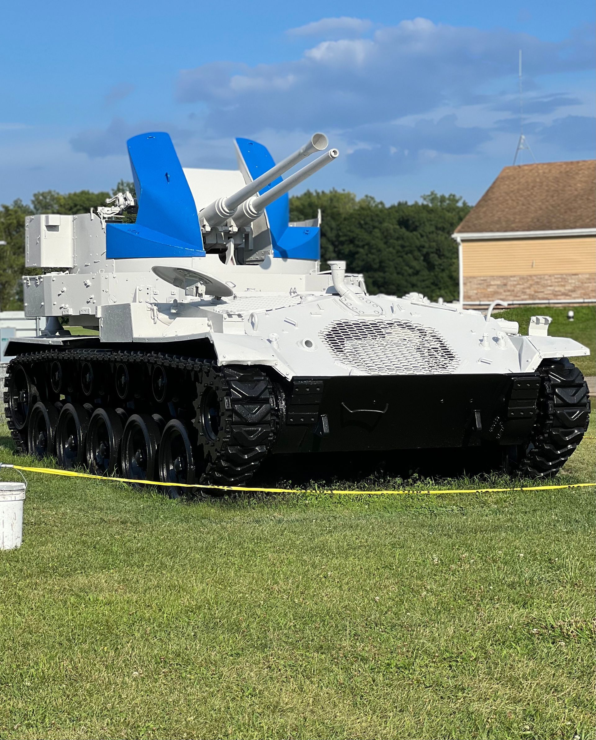 A white tank with a blue wing is parked in a grassy field.