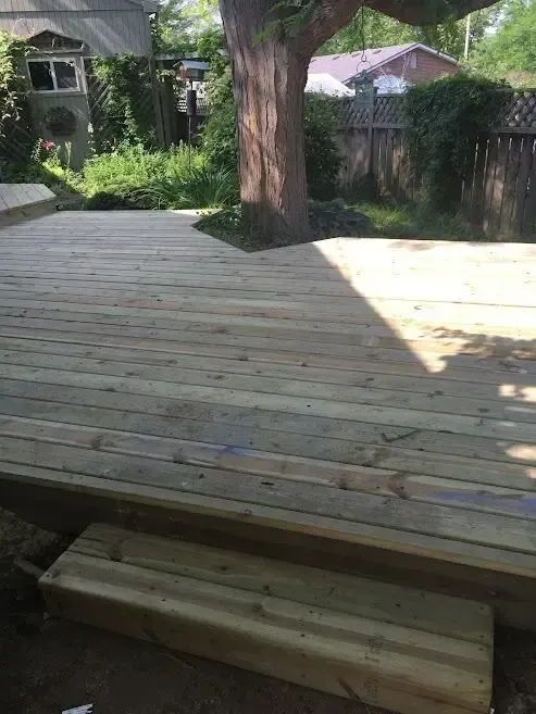 A wooden deck is being built in a backyard with a tree in the background.