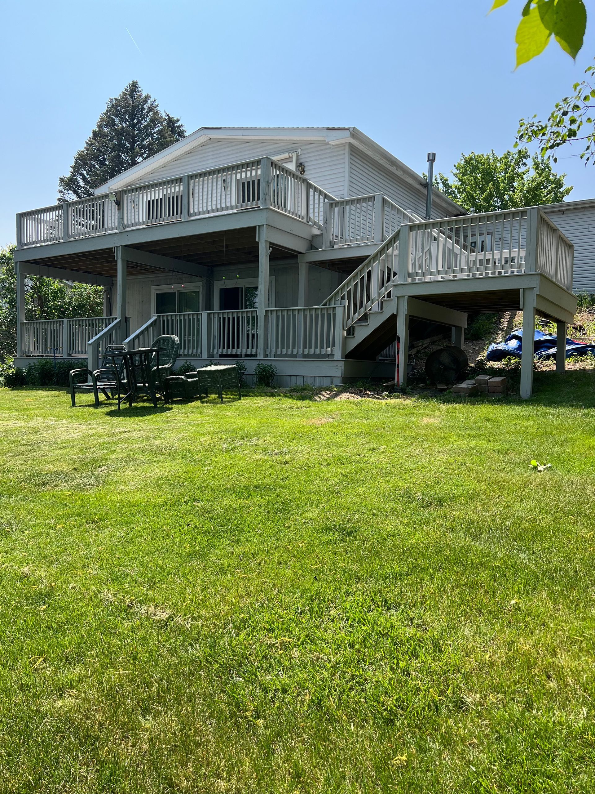 A house with a large deck and stairs is sitting on top of a lush green field.