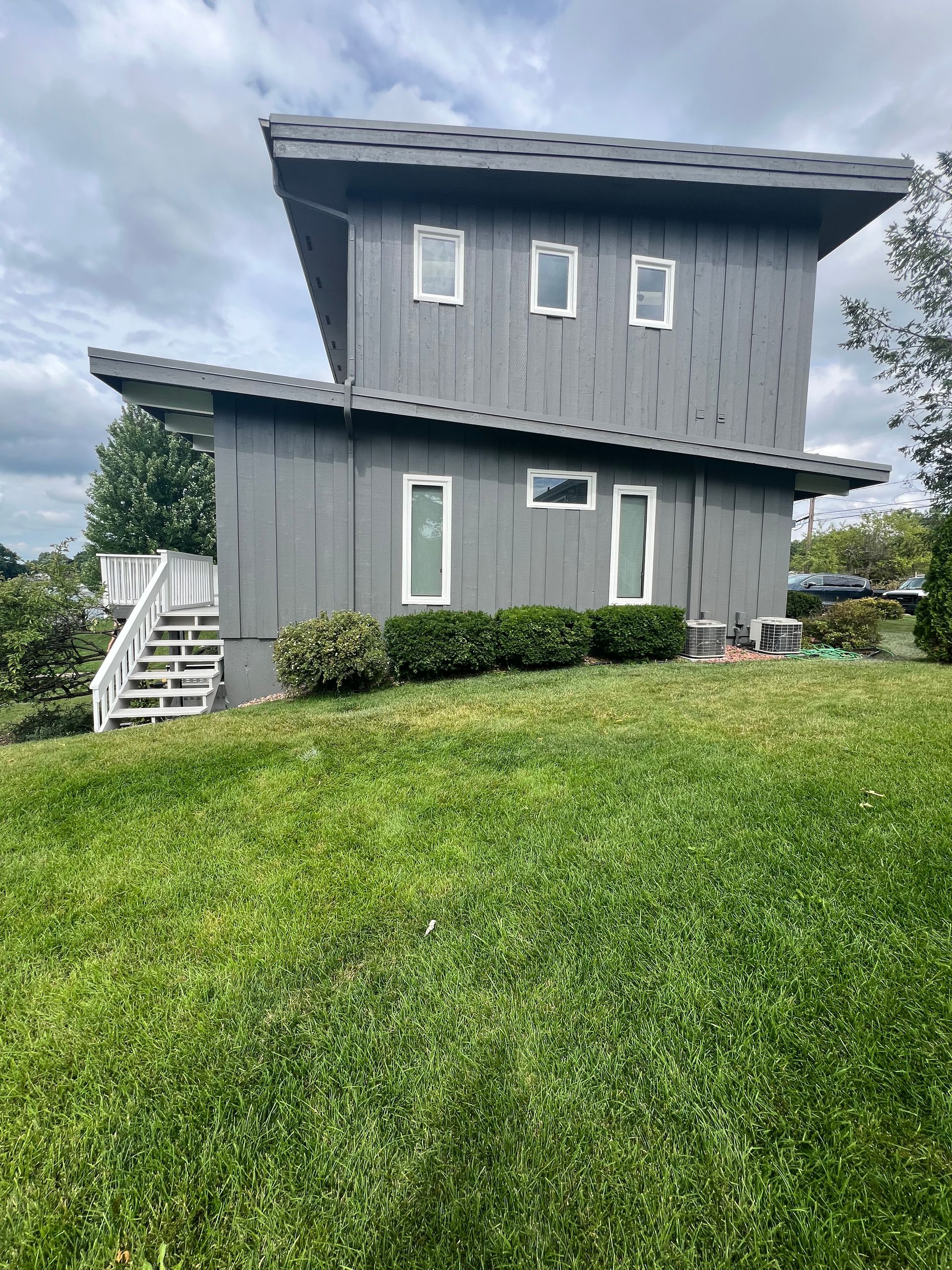 A large gray house is sitting on top of a lush green hill.