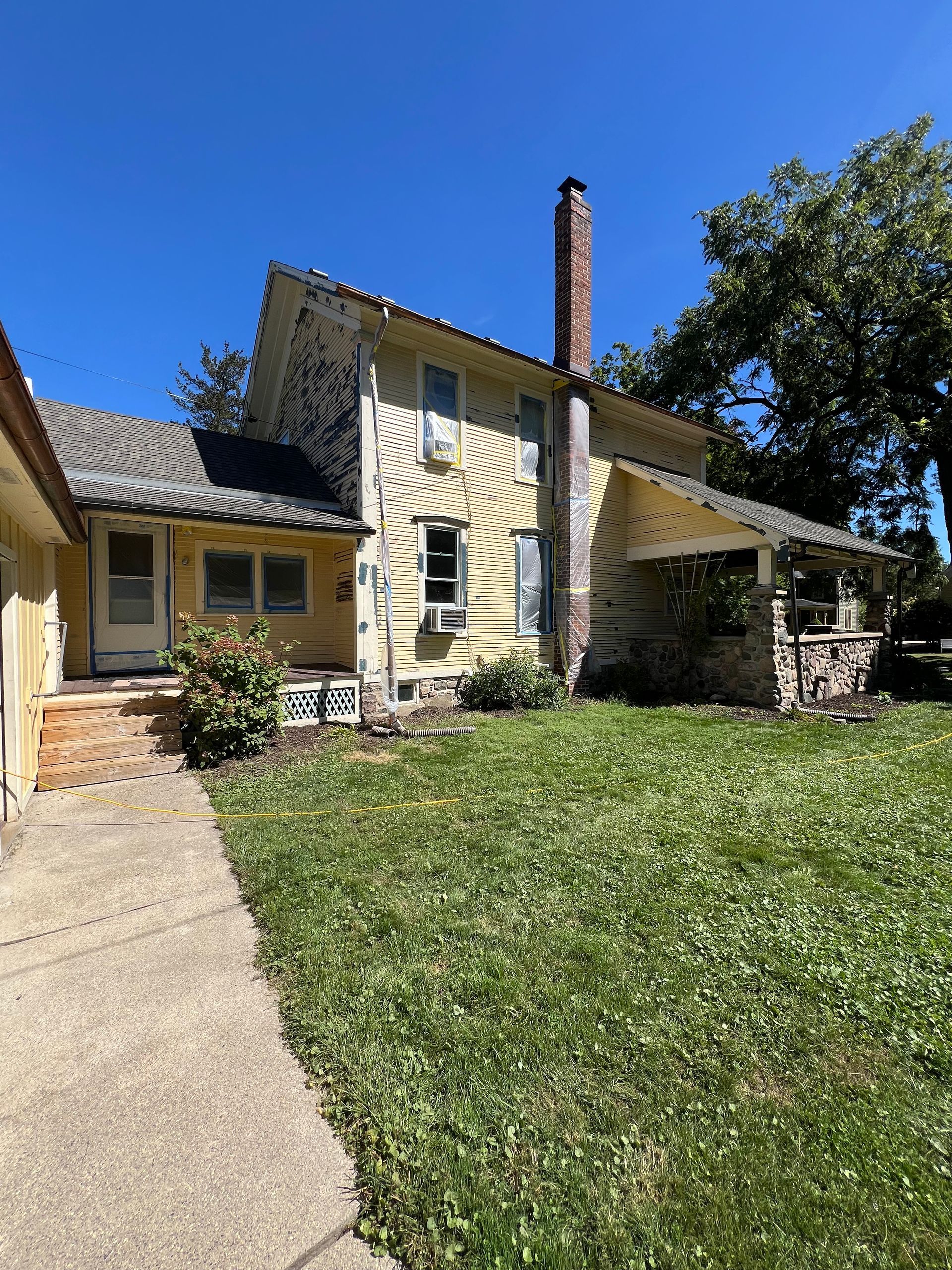 A large yellow house with a brick chimney is sitting on top of a lush green lawn.