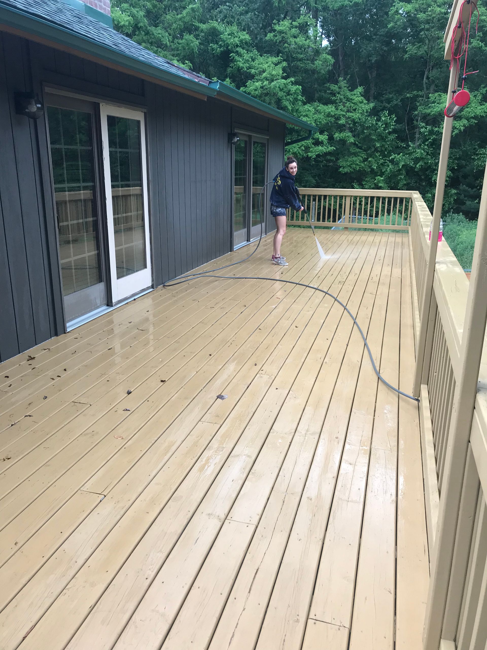 A woman is cleaning a wooden deck with a hose.