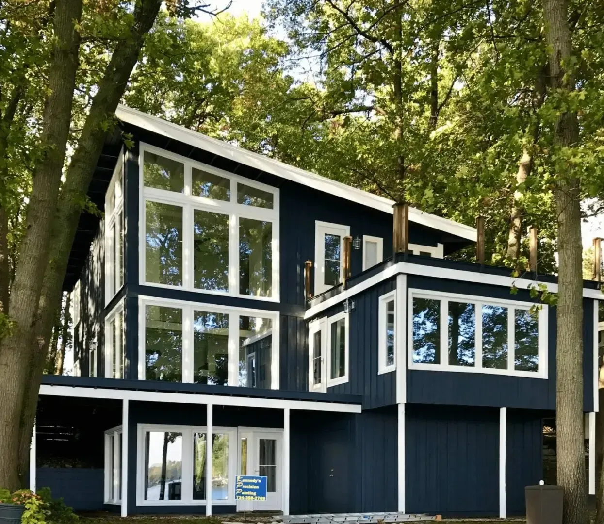 A large blue house with lots of windows is surrounded by trees.
