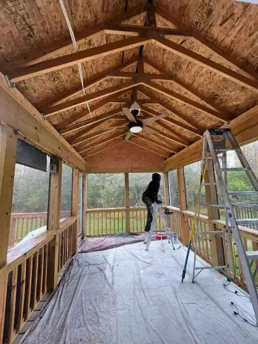 A man is standing on a ladder in a screened in porch.