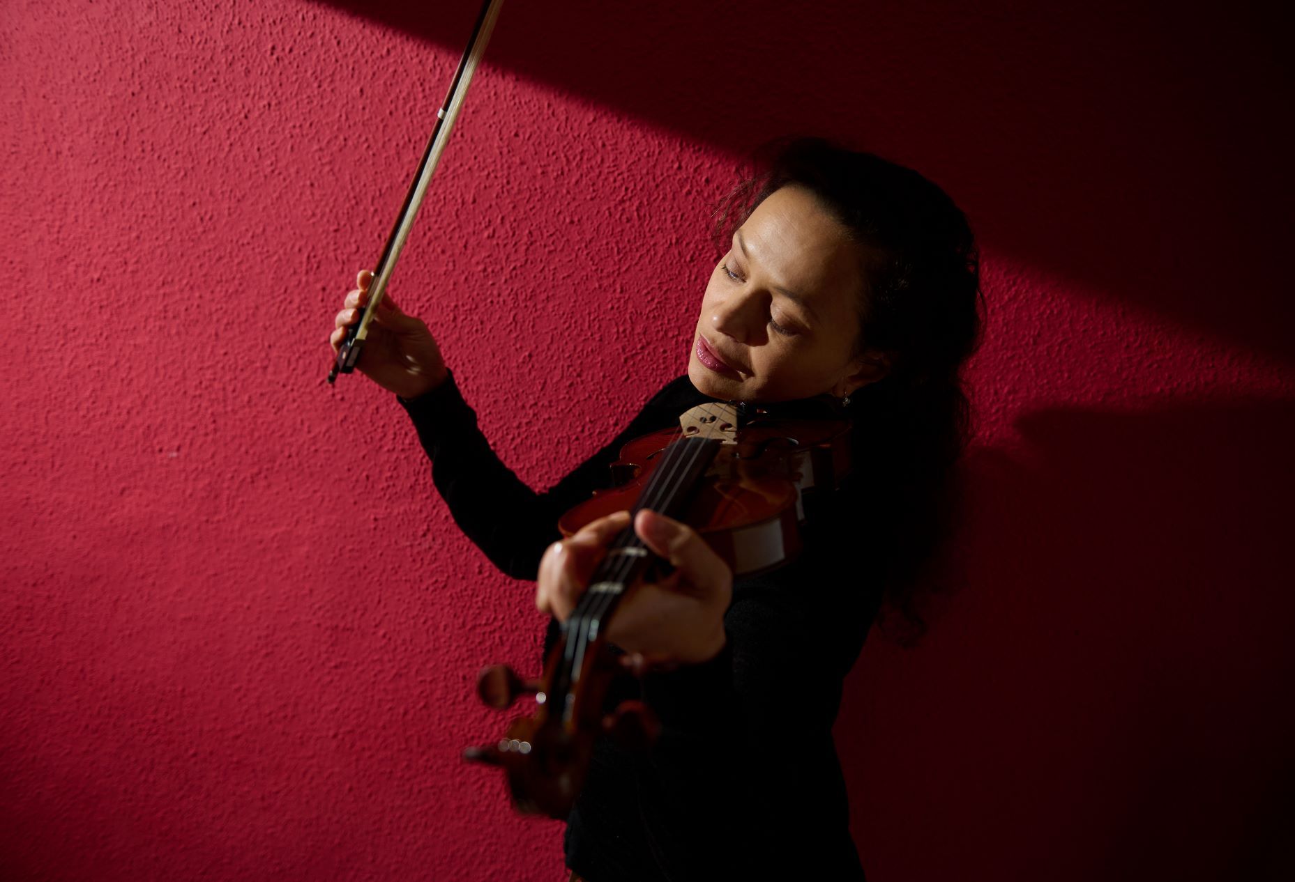 A woman is playing a violin in front of a red wall.