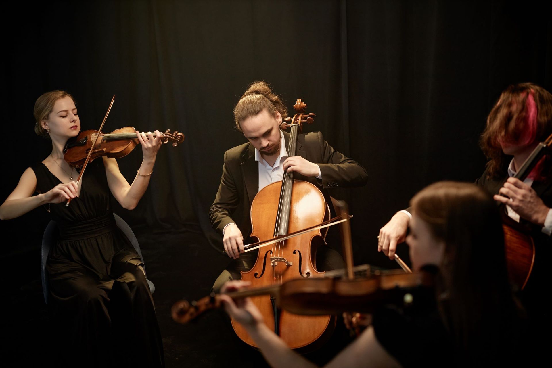 A group of people are playing violins and cello in a dark room.