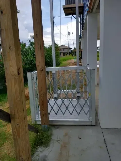 A white gate is sitting on the side of a building next to a wooden post.
