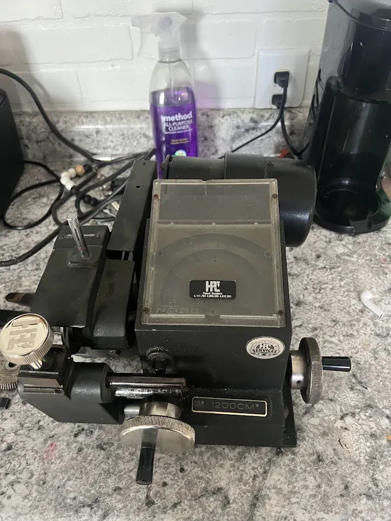 Black key cutting machine on a countertop, with a purple cleaning spray and a coffee maker visible.