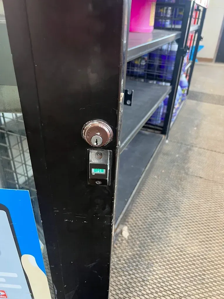 Black cabinet with key lock and digital display in store aisle. Empty shelves behind.