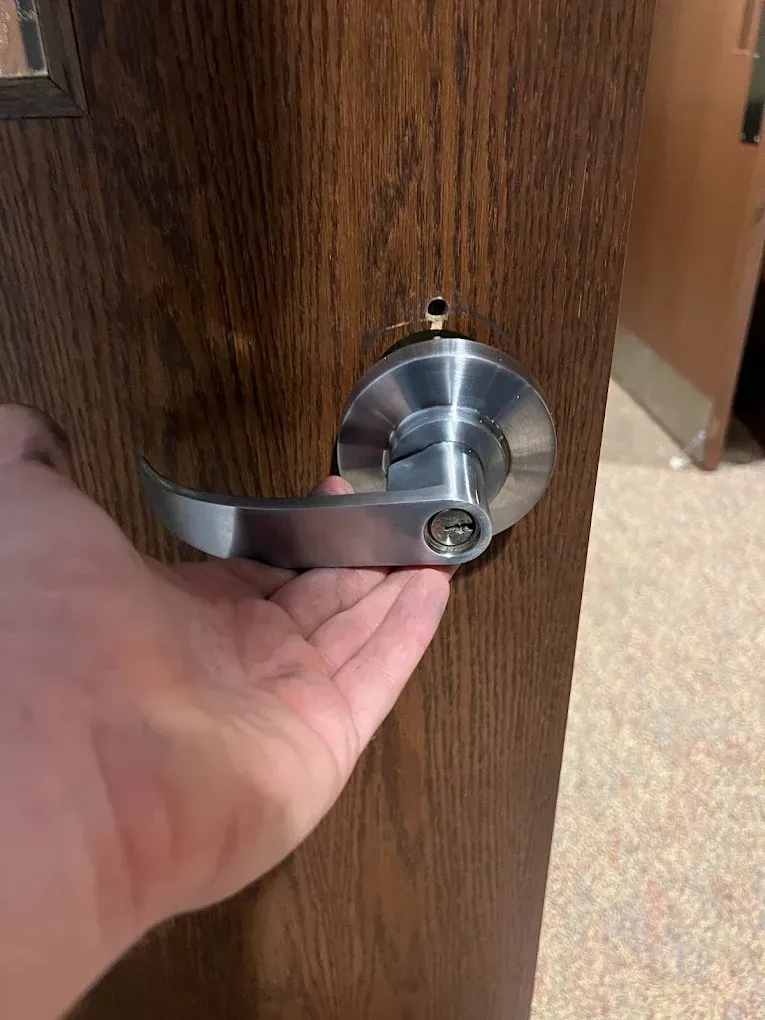 Hand holding a lever door handle on a wooden door.