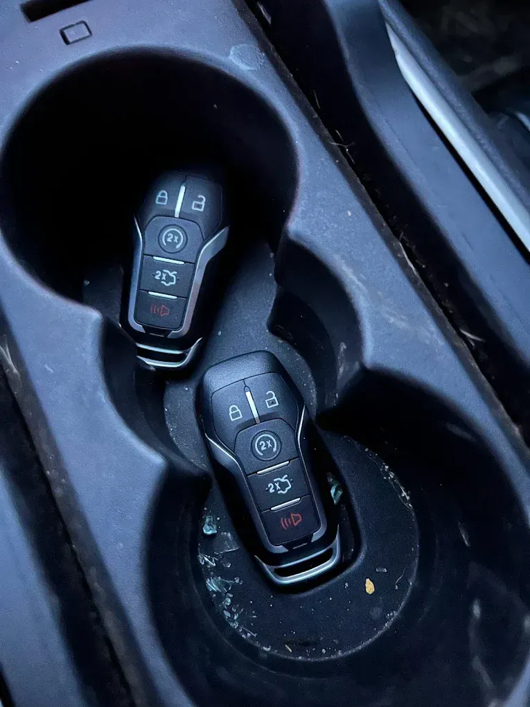 Two black car keys in a dark, dirty car cup holder.