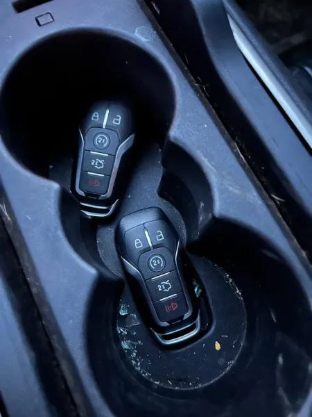 Two black car keys in a dark, dirty car cup holder.