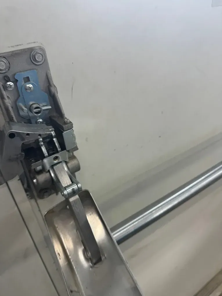 Close-up of a metal door latch mechanism with a silver handle and a silver rod mounted on a white wall.
