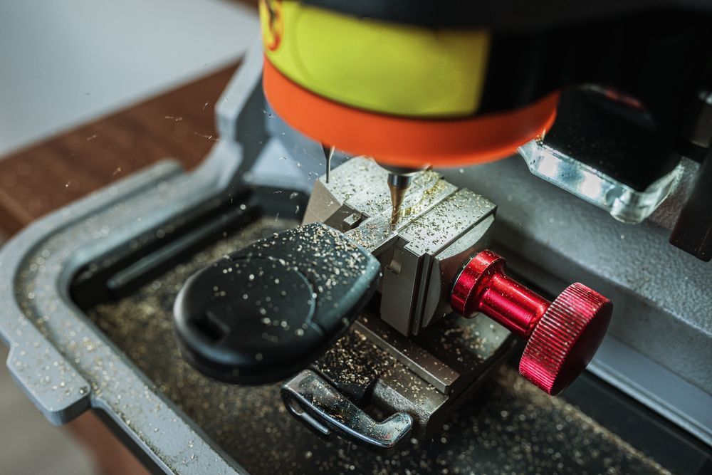 Key-cutting machine in action, cutting a car key. Sparks and metal shavings visible.