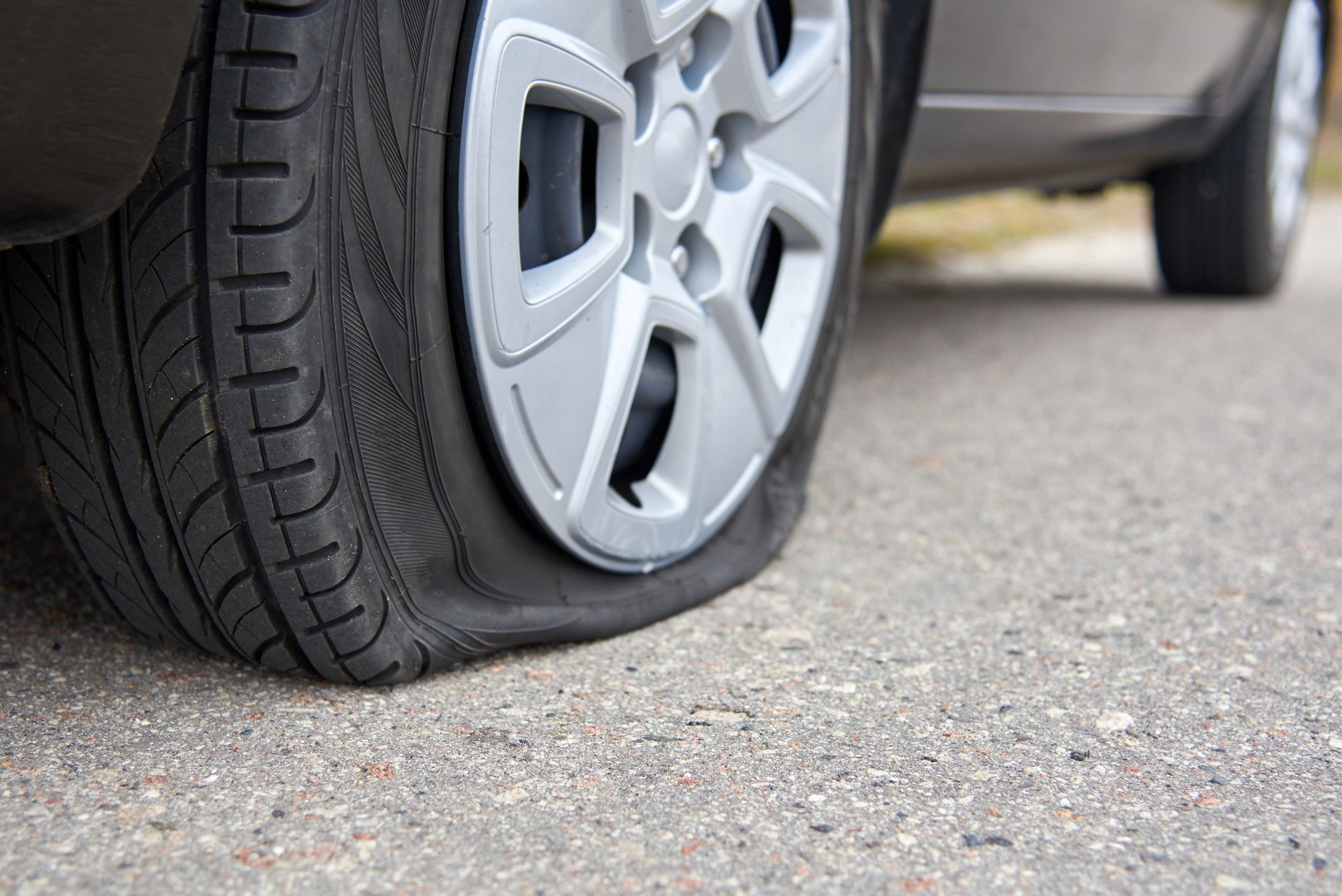 Flat tire on a gray car parked on a paved road.