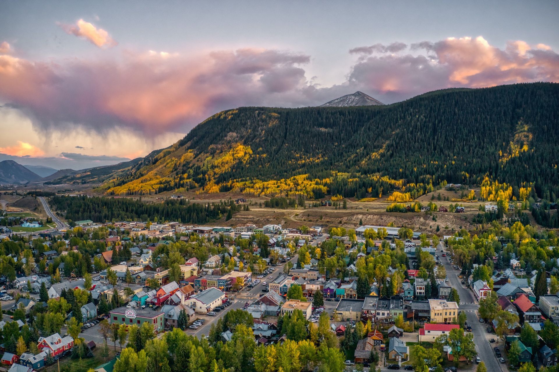 Town nestled in a valley with mountains under a sunset.