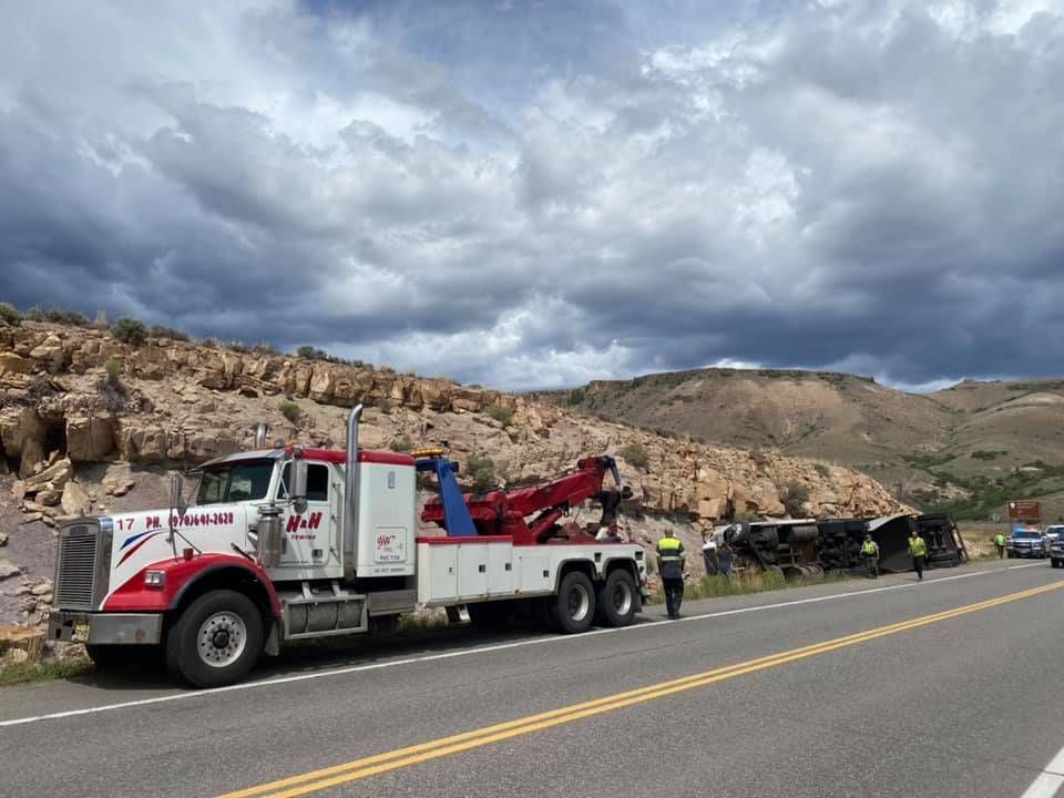 Tow truck next to a crashed vehicle on a roadside with a rocky hill backdrop.
