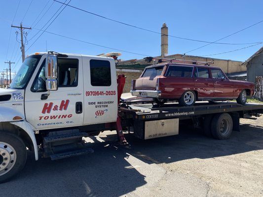 A red station wagon on a flatbed tow truck labeled