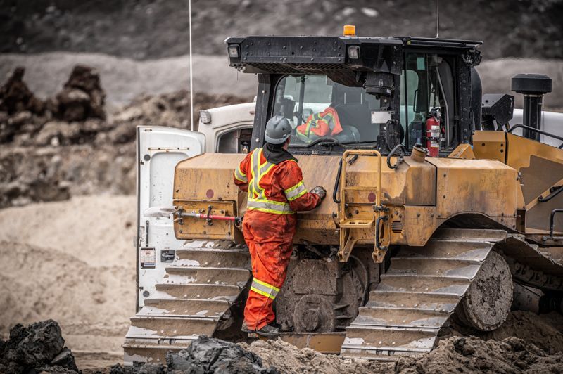 A man is standing next to a bulldozer in a dirt field.