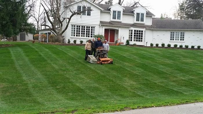 A group of people are mowing a lush green lawn in front of a house.