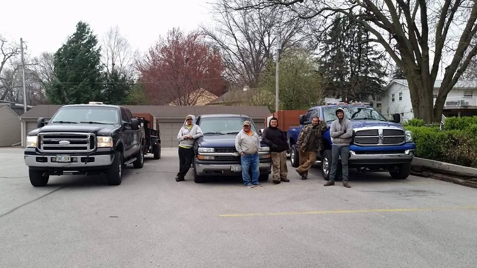 A group of men are standing in front of trucks in a parking lot A group of men are standing in front of trucks in a parking lot