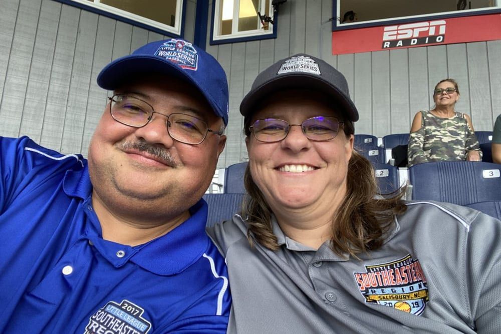 A man and a woman are posing for a picture at a baseball game.