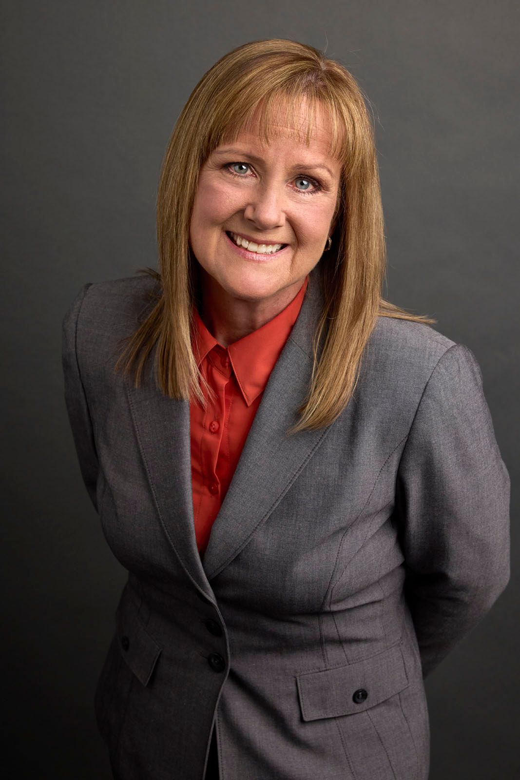 A woman in a suit and red shirt is smiling for the camera