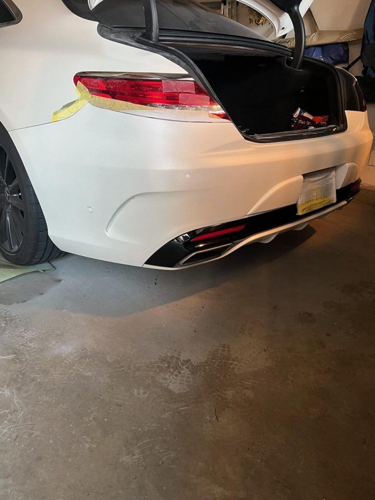 A white car parked in a garage with yellow masking tape applied to the body near the tail light.