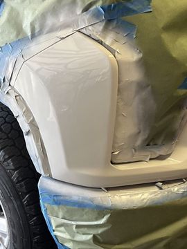 A car body panel painted off-white, partially masked with tape and protective paper during a repair or painting process.