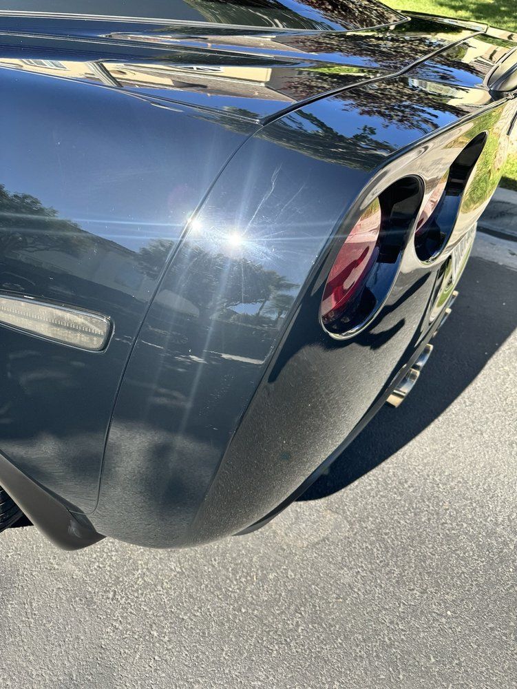 Close-up of the rear corner of a dark-colored Chevrolet Corvette showing the taillight and body panel on asphalt.