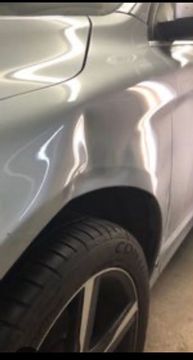 A shallow, elongated dent on the silver front fender of a car, positioned just above the wheel arch.