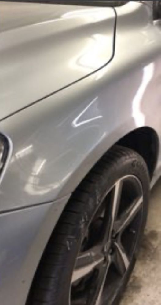 A close-up of a silver car's front fender and wheel, showing the smooth paint finish and part of a dark alloy wheel.
