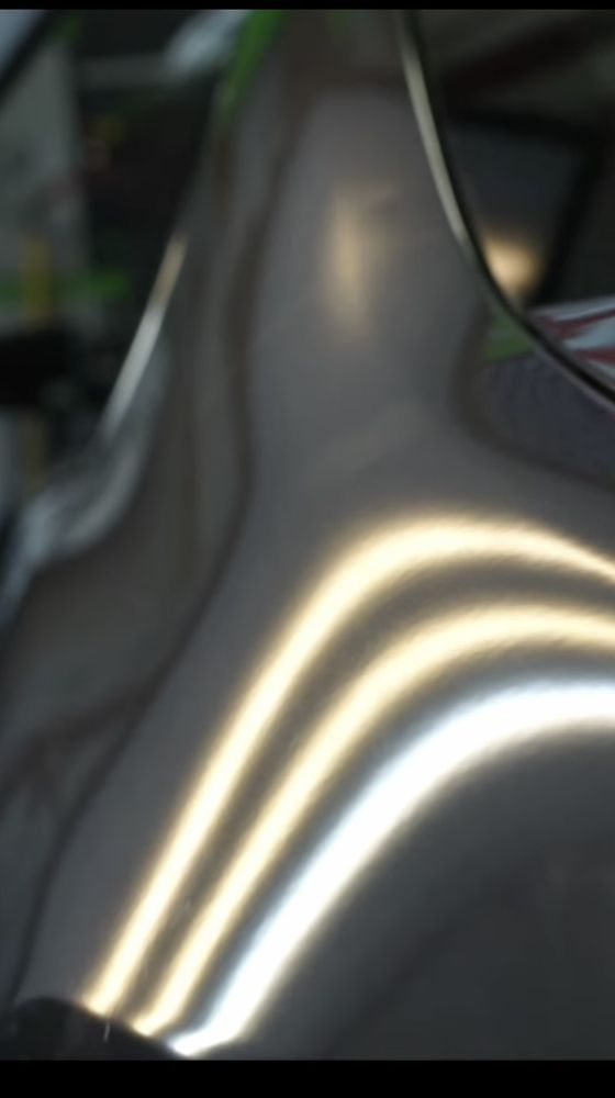 Close-up of a smooth, dark automotive surface reflecting bright, parallel light stripes from a PDR inspection lamp.