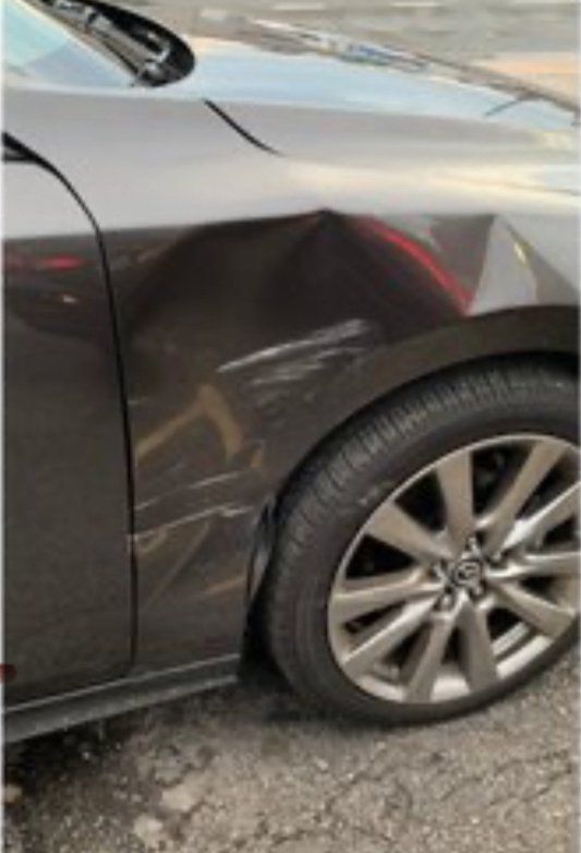 A side view of a dark grey car showing a dent and surface scratches on the front passenger-side fender.