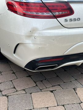 A white Mercedes-Benz S 550 showing a noticeable dent and paint damage on the rear bumper.